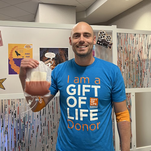 Stem cell donor Bobby Alexis in Gift of Life's collection center holding up the bag of stem cells he donated to save Aidan Samoon's life. 
