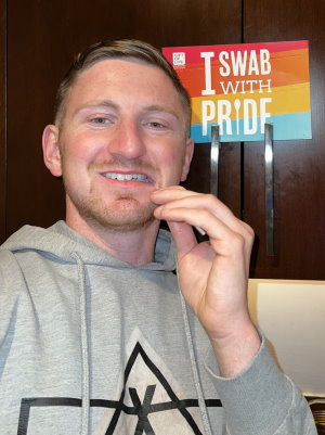 Cale, a student at Georgetown University, donated stem cells to save a life. In this photo he is shown using a swab to get a tissue sample from inside his cheek to demonstrate how to use a  Gift of Life Marrow Registry swab kit.  Cale participated in the "Swab With Pride" campaign in June 2022 to recruit LGBTQ+ donors to the registry, and a sign hangs behind him saying "I Swab With Pride".