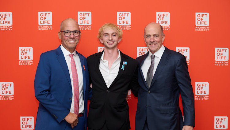 (L-R) Leukemia survivor Mark Josephson, his stem cell donor Jacob Isrow, and Birthright Israel Foundation Chairman of the Board Philip de Toledo. Mr. Josephson is wearing a blue suit with a white shirt and mauve tie, and is balding with glasses. Jacob Isrow is wearing an open collared white shirt and black suit, and Philip deToledo wears a dark navy suit, white dress shirt and gray necktie. They stand in front of a Gift of Life backdrop covered with logos. 