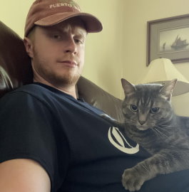 Gift of Life stem cell donor Matt, a sandy haired man in his 20s, is relaxing at home in a large chair with his gray tabby cat Sammy on his lap. 