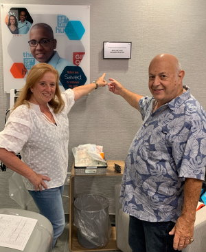 In Gift of Life Marrow Registry's stem cell collection center, Ed Muster and his daughter Kim Delprete are smiling and pointing at a new plaque on the wall. Ed and his wife Adeline made a contribution to fund this donor suite, and the plague commemorates their generous contribution. 