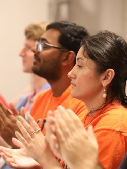 A row of Gift of Life Campus Ambassadors is sitting at a table in a meeting room and applauding a speaker who is not pictured. 