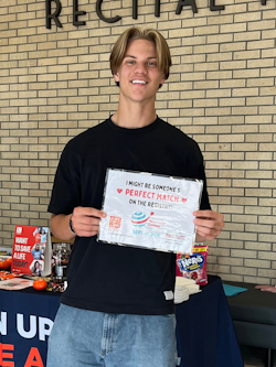 A Gift of Life Campus Ambassador who is manning a swabbing table at a university takes a moment to hold up a World Marrow Donor Day placard. 
