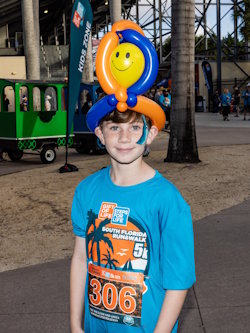 A boy sporting a smiley face balloon hat and a Steps for Life running shirt is preparing for the 5k event on January 25, 2026.