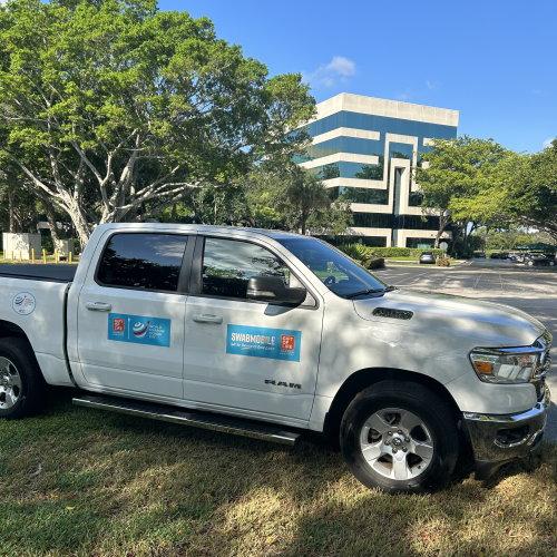 Gift of Life's "Swabmobile" truck is shown in front of the headquarters building, with large Florida live oak trees in the background. 