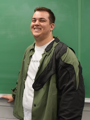 Gift of Life Marrow Registry donor Owens is a student at the University of Florida. He is shown in a green jacket and backpack standing in front of a blackboard. He recently donated blood stem cells to save the life of a man battling to survive leukemia. 