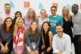 A diverse group of office staff, including one in a Gift of Life shirt, are smiling at the camera after a presentation about stem cell and marrow donation at their office.