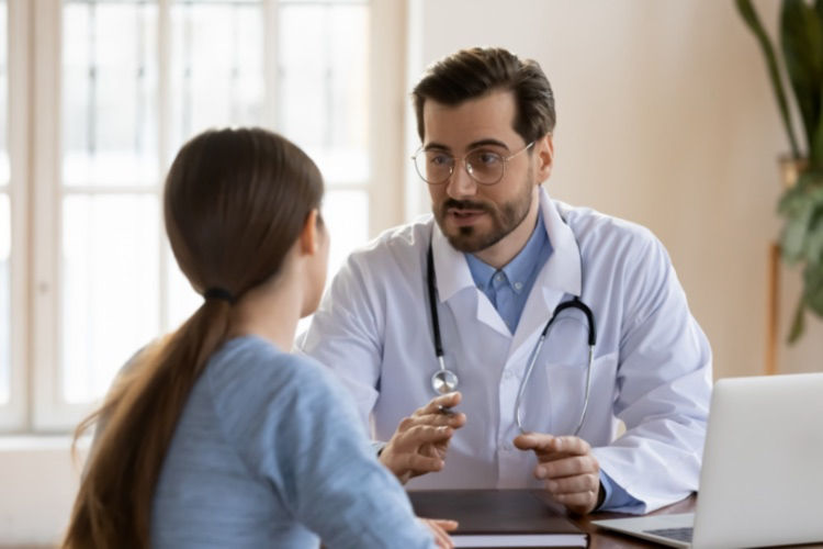 A young woman is facing away from the camera and talking to a doctor, who has a serious expression on his face.