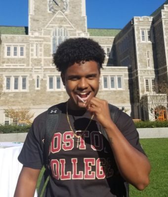 A smiling, Black, male college student wearing a Boston College tee shirt is using a cheek swab as he completes a Gift of Life Marrow Registry swab kit.