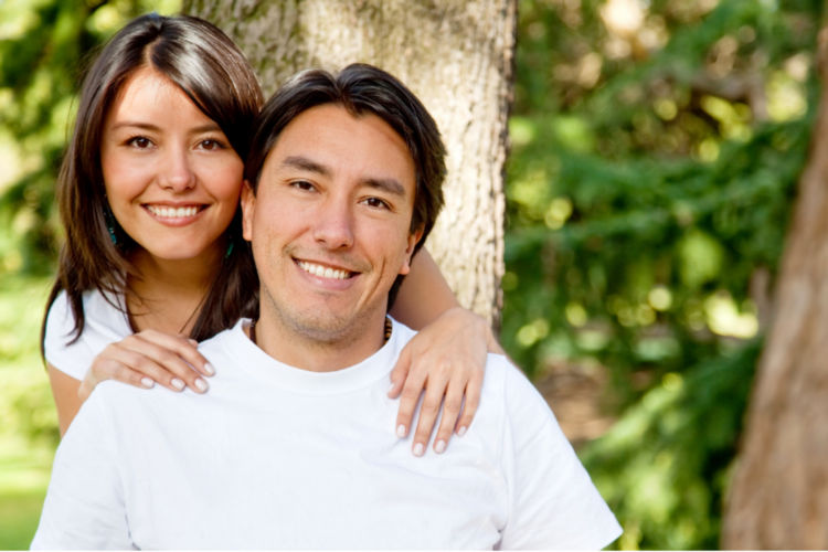 A Hispanic brother and sister in their late 20s are smiling and looking into the camera.