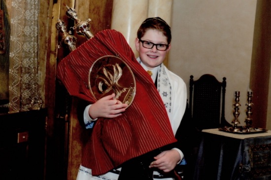 A smiling young man is shown proudly holding the Torah at his Bar Mitzvah ceremony. Many young men and woman perform charitable works for Gift of Life in preparation for their bar/bat miztvah ceremonies.