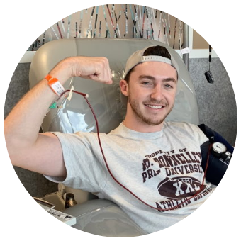 Matt is shown in Gift of Life's collection center donating cells for a research project. He has a big smile and is doing a bicep curl with his right arm. He is dark-haired and fair-skinned, and is wearing a backwards baseball cap and a football tee shirt.
